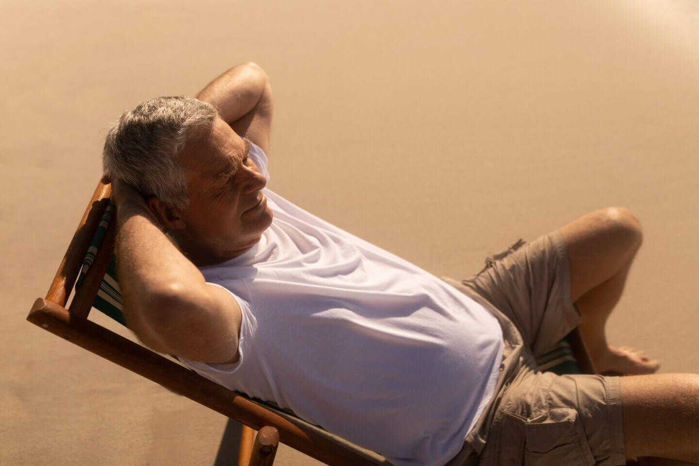 vue arrière de l'homme senior actif-détente-avec-mains-derrière-la-tête-sur-le-lit de soleil-à-laplage